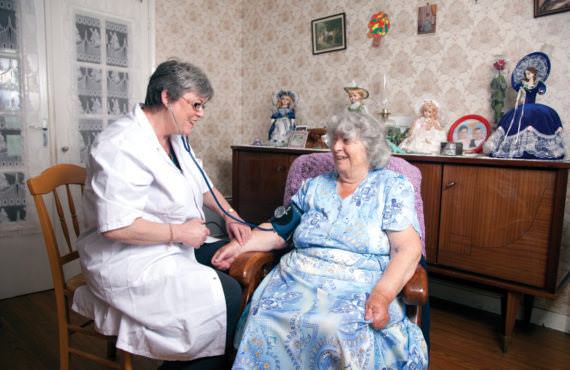Une infirmière prend la tension d'une personne âgée. Elles sont toutes les deux assises.