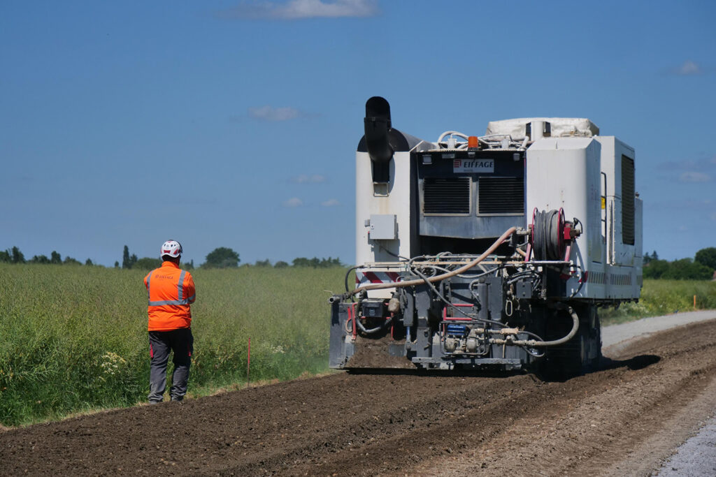 RD547-2 grosse machine en train de racler une route et une personne avec un gilet orange