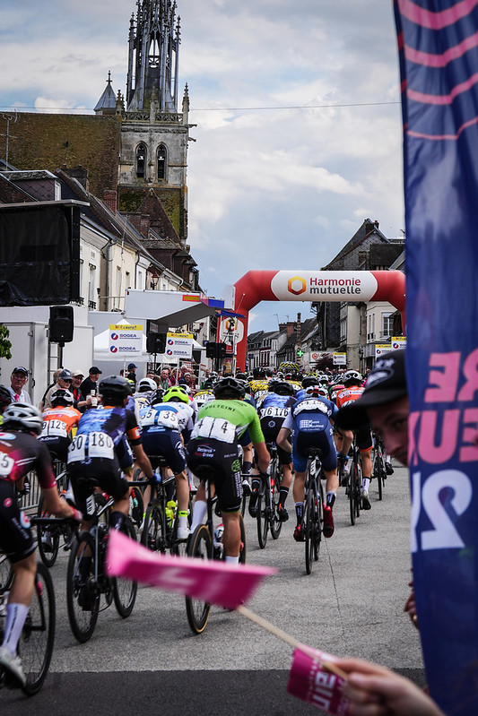 tour-eure-juniors-2024-2 peloton de cyclistes avec une église en arrière plan